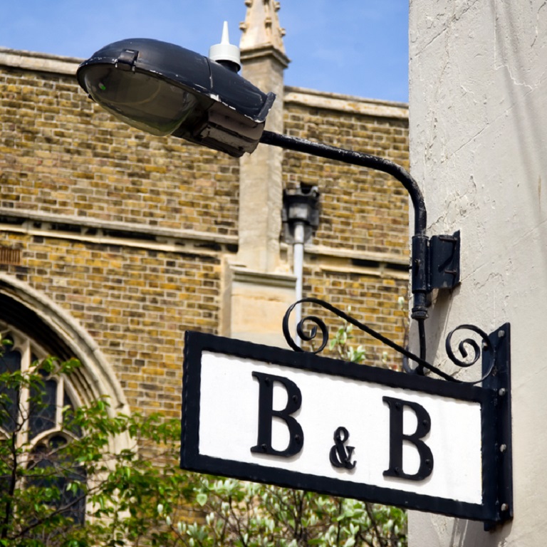 A sunny B&B (Bed & Breakfast) sign on a building near a church in England.