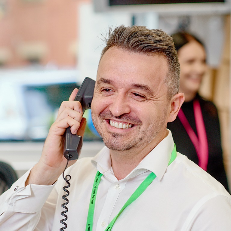 Customer service agent holding phone and smiling with colleagues in the background