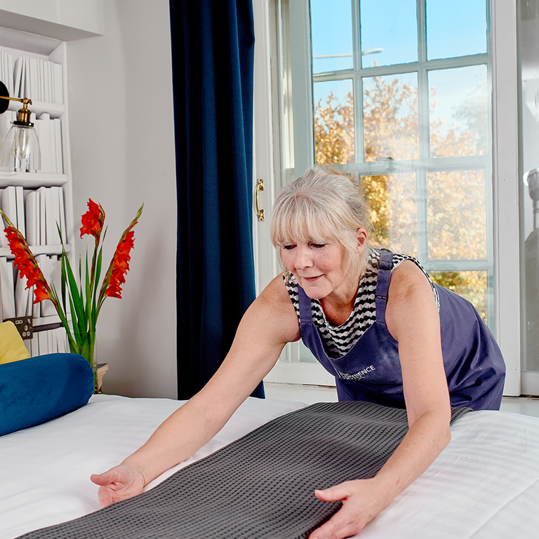 A hotel staff member arranging bedding in a well-decorated room, showcasing a stylish and inviting atmosphere to attract potential guests.