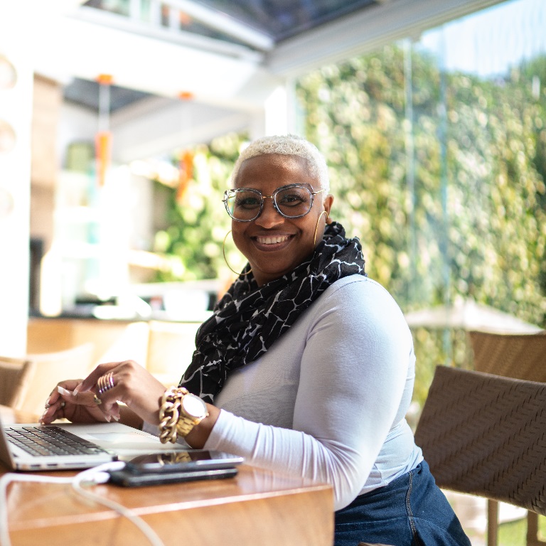 Person typing on a laptop at a wooden table in a bright office space with large windows and greenery outside, illustrating focused work related to Autumn Budget 2025