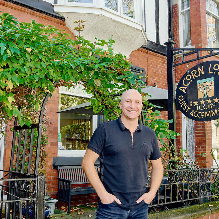 Man smiling and standing with hands in pocket in front of Acorn Lodge guesthouse 